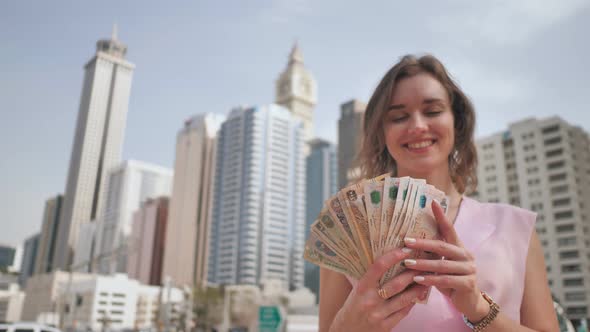 The Girl Holds in Her Hands the Money of the United Arab Emirates on the Background of the City