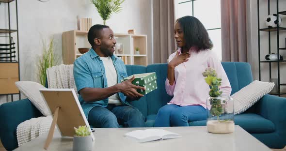 African American Couple Sitting Together on the couch at home and giving each other gift boxes