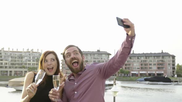 Couple posing for selfie while drinking champagne outdoors