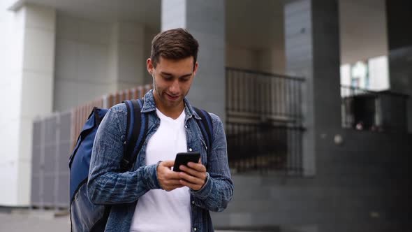 Medium Shot Portrait of Cheerful Delivery Man with Thermo Backpack Using Navigation App on