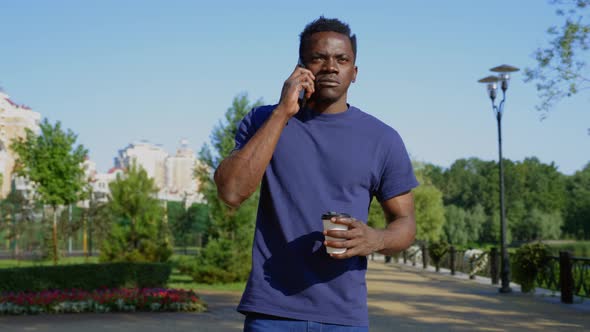 Afroamerican Man Uses Mobile Phone Holding White Cup with Coffee or Tea in Hand