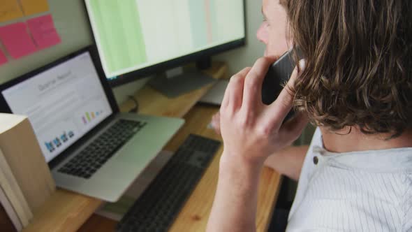 Focused caucasian man working remotely, using laptop and talking on smartphone