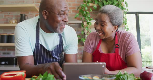 Happy african american senior couple cooking together, using tablet in kitchen