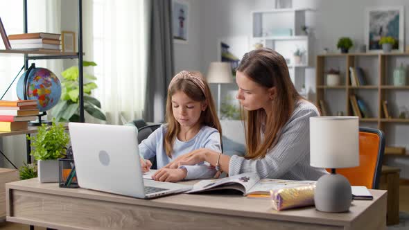 Mom Helps Daughter with Homework at Home in Living Room