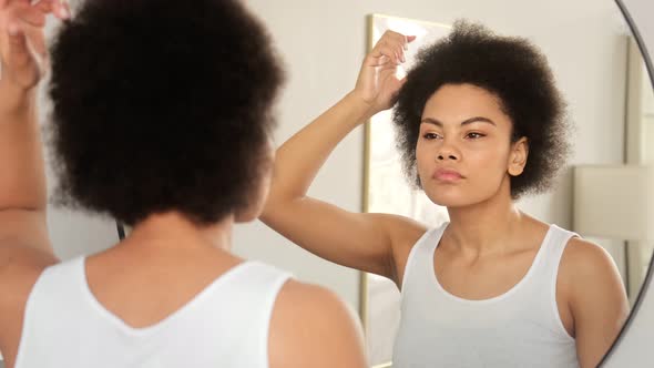 African american woman applies hair care balm styling cosmetics, makes hairstyle