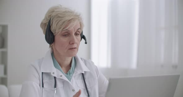 Aged Female Family Doctor Is Consulting Online, Talking with Patient By Video Chat at Laptop