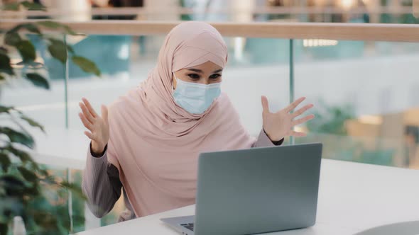 Surprised Arab Woman Wearing Medical Mask Looking at Laptop Screen Receiving Email Reading Good News