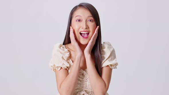 Happy attractive asian young woman excited surprised open mouth and touching her cheek