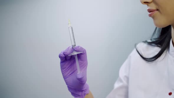 A beautician in purple gloves is holding an injection of a botulinum toxin in her hand