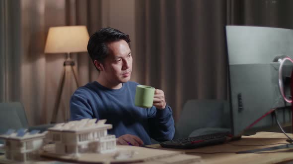 Asian Male Engineer With The House Model Drinking Coffee While Working On A Desktop At Home
