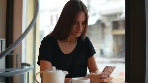 Attractive Young Lady with Natural Makeup Using Her Mobile Phone in the Coffee Shop