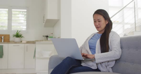 Happy asian woman sitting on sofa, resting with laptop at home