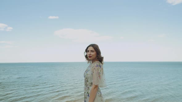 A Woman Look at Camera and the Sea and White Clouds Merge with the Water on the Horizon on the