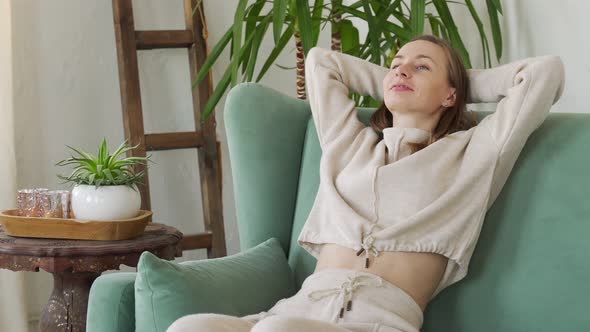 Tired Young Woman Is Resting in a Comfortable Chair with Her Hands Behind Her Head