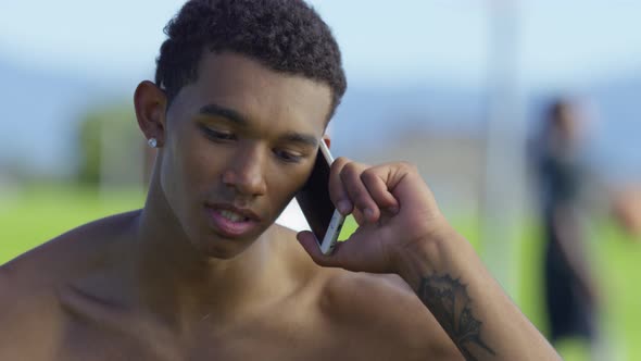 Teen basketball player talking on cell phone at outdoor court