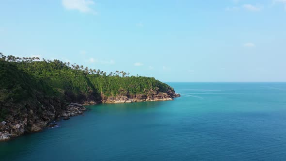 Beautiful rocky elevated coast with palms in the calm ocean. Thailand