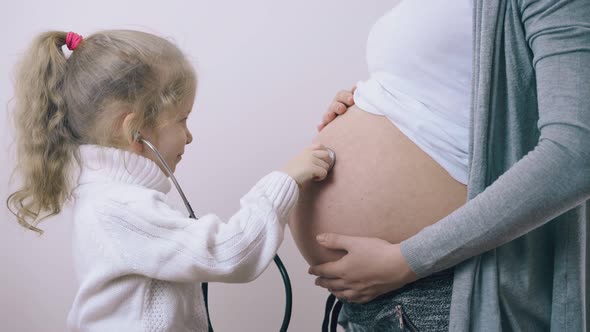 Little Child Touches Pregnant Mom Belly with Stethoscope