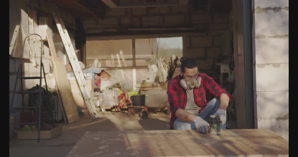 A Man in a Respirator Goggles Polishes a Parquet Board with an Orbital Sander