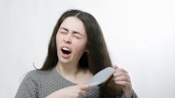 A Young Tired Woman Combs Her Hair Yawns and Falls Asleep Standing Up with a Comb in Her Hair