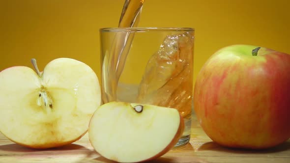 Apple Juice Is Poured in a Glass Next To Large Apples on the Yellow Background