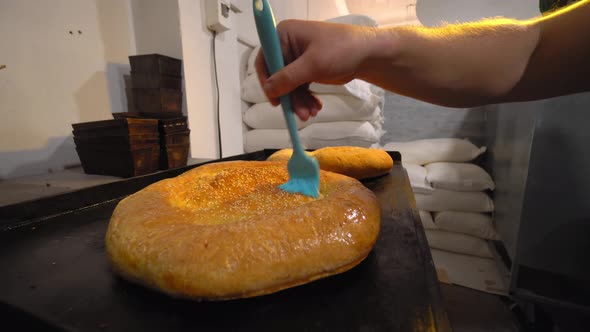 a cook combing melting butter with brush on baked bread