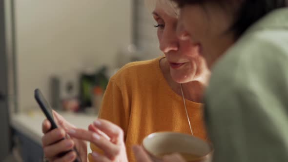 Positive mature women looking at phone with her friend