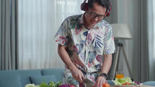 Happy Asian Man Listening To Music With Headphones And Singing While Cooking Healthy Food