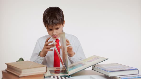 Curious School Kid in Red Tie Sitting at Table Folding Pages of Geographic Atlas with Interest on / Videohive, Stock footage, Education
