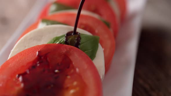 Camera follows pouring balsamic vinegar over tomato and mozzarella cheese salad. Slow Motion.