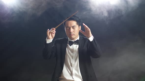 Asian Conductor Man Holding A Baton Closing His Eyes And Showing Gesture In The Black Studio