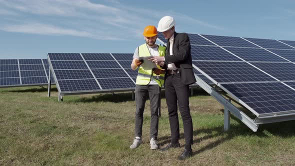 The Businessman and Worker Are Discussing Documents Standing Near Solar Batteries Outside