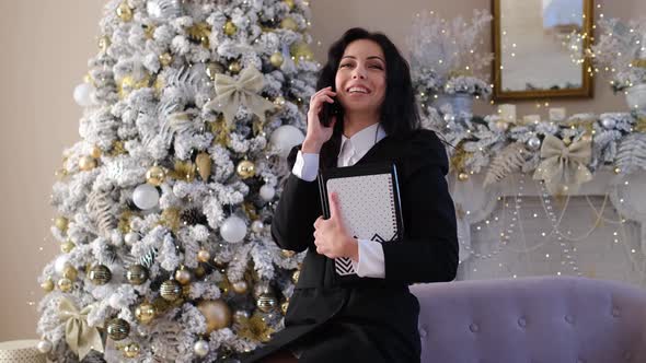 Happy Businesswoman in Room with Christmas Tree Chatting on Cellphone