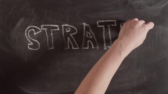Word strategy is written in bulk letters on a chalkboard, timelapse. Concept of a work plan