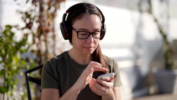 Adult Woman is Using Smartphone and Listening to Music By Wireless Headphones Sitting in Cafe