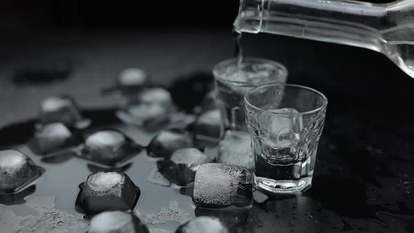 Pouring Up Shots of Vodka From a Bottle Into Glass. Black Background