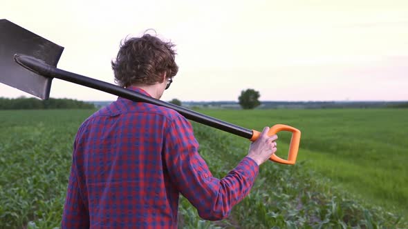 The farmer holds a shovel in his hand on an agricultural field, harvest time.