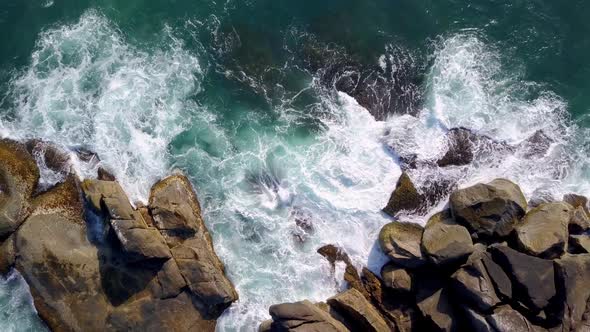 Aerial top down shot of waves breaking on the boulders in Trilha da Sepultura, Bombinhas. Jib up