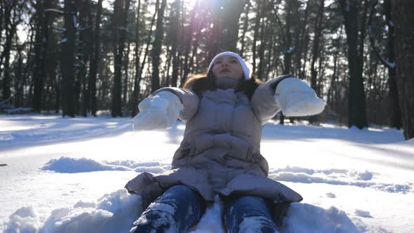 Young Girl in Winter Clothes Playing on Snowy Meadow at Sunny Day. Portrait of Happy Woman Throwing