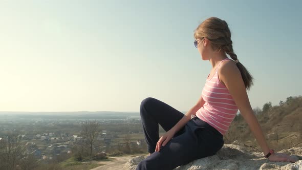 Young relaxed woman sitting outdoors on a big stone enjoying warm summer day. Girl meditating 