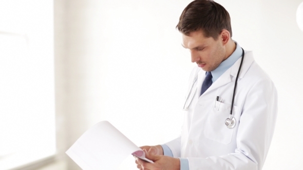 Male Doctor Reading Medical Documents At Hospital