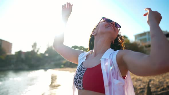 Young Happy Woman in Sunglasses Tossing Hair in Slow Motion Standing in Sunbeam on Mediterranean Sea