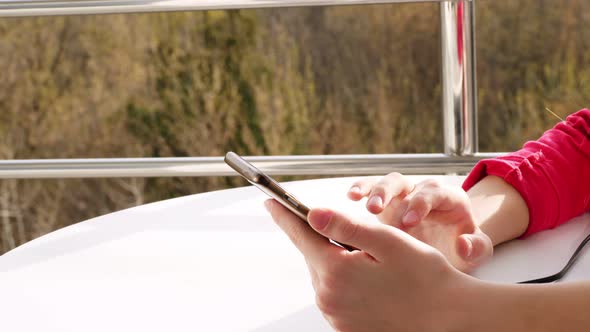 Close-up of Hands, Teenager Girl Uses Smartphone,on Open Balcony. Spring Sunny Day.