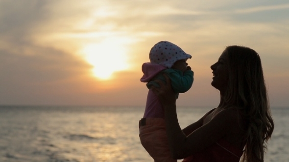 Silhouette Of Mother Kissing Baby At Sunset Near