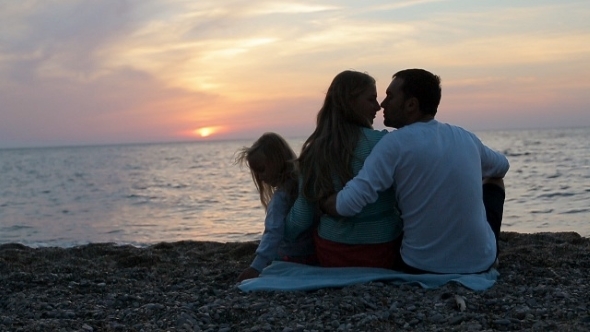 Happy Family Sitting In The Sunset Near The Sea In