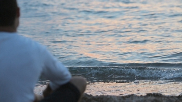 Man Sitting Near The Sea And Throwing Stones Into