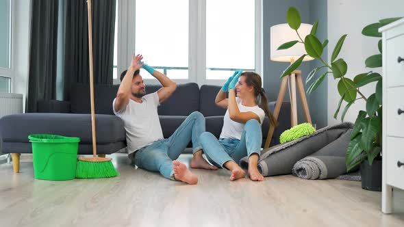 Tired Couple Sits on the Floor in a Room and High Five Each Other After They Finish Cleaning the