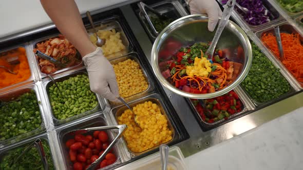 Worker assembles colorful salad at vegetable station in restaurant, slow motion slider 4K