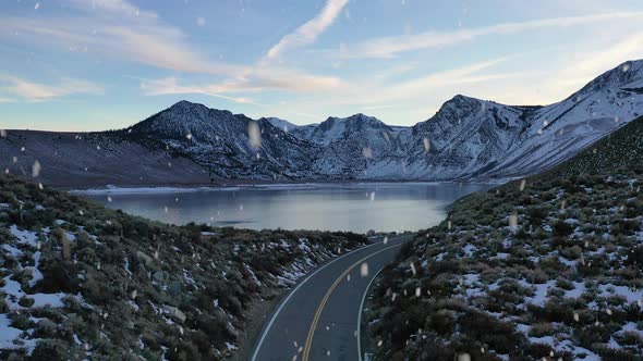 Beautiful mountain road with reveal of lake during winter season and snowfall, aerial ascend view