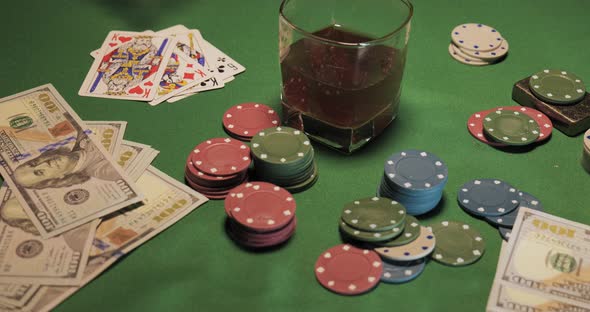 Chips Cards a Glass of Whiskey and Money are on the Green Gaming Table