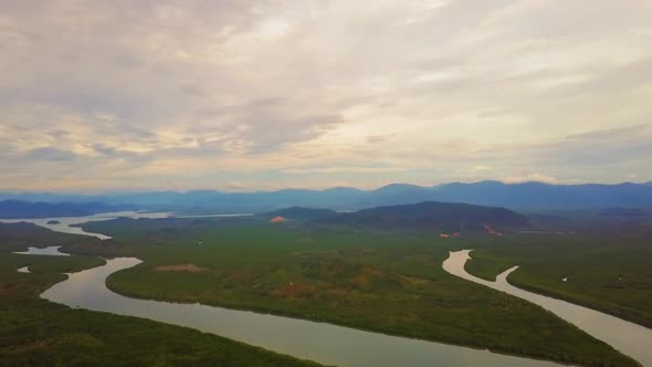 Panning drone view of landscape of a river in a valley with mountains in the background on a cloudy